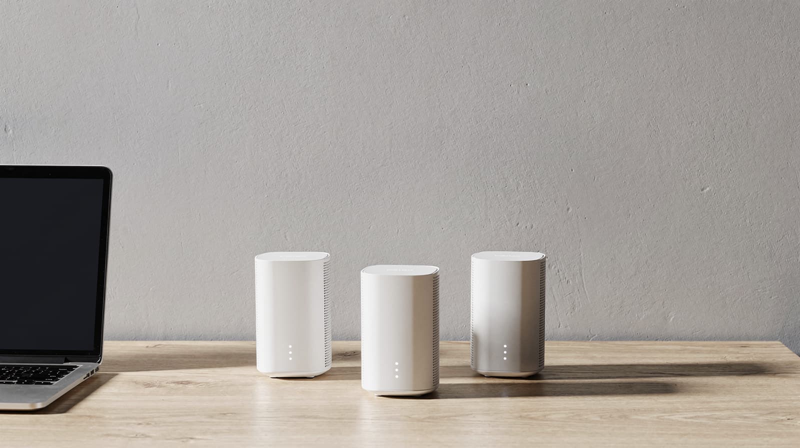 Three white mesh Wi-Fi nodes on a minimal desk beside a laptop