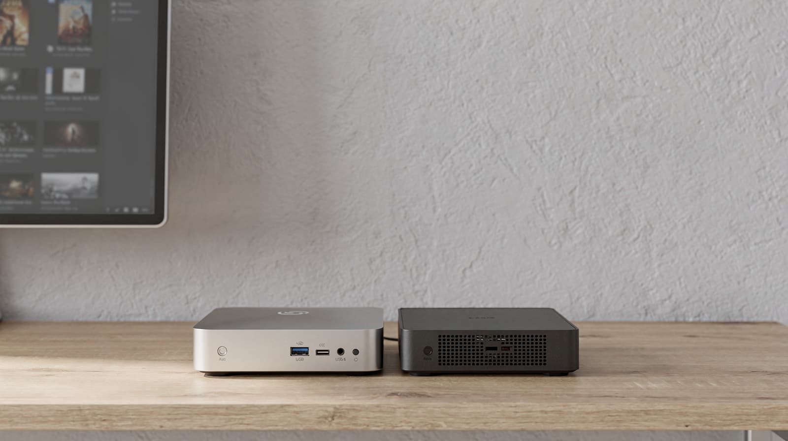 Two compact mini PCs on a desk beneath a media-library screen