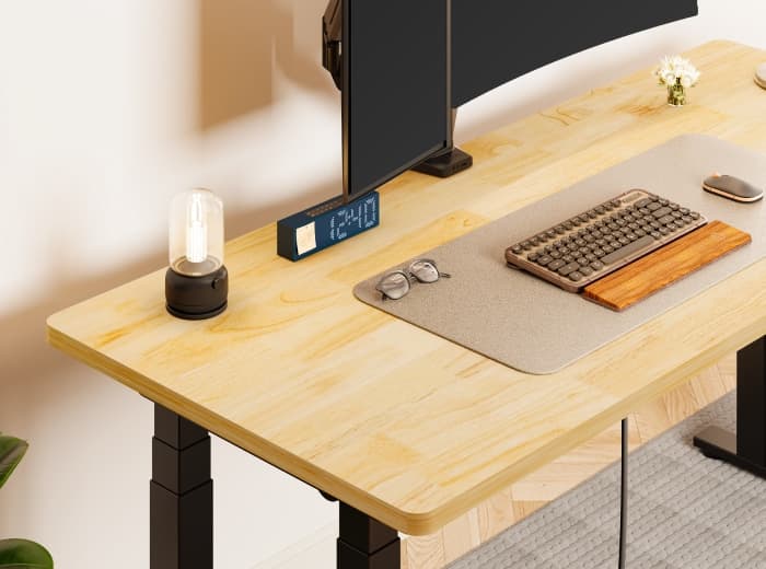 Light wood desktop of a FlexiSpot E7 Plus standing desk with a monitor on an arm, a keyboard, a mouse pad and a lamp