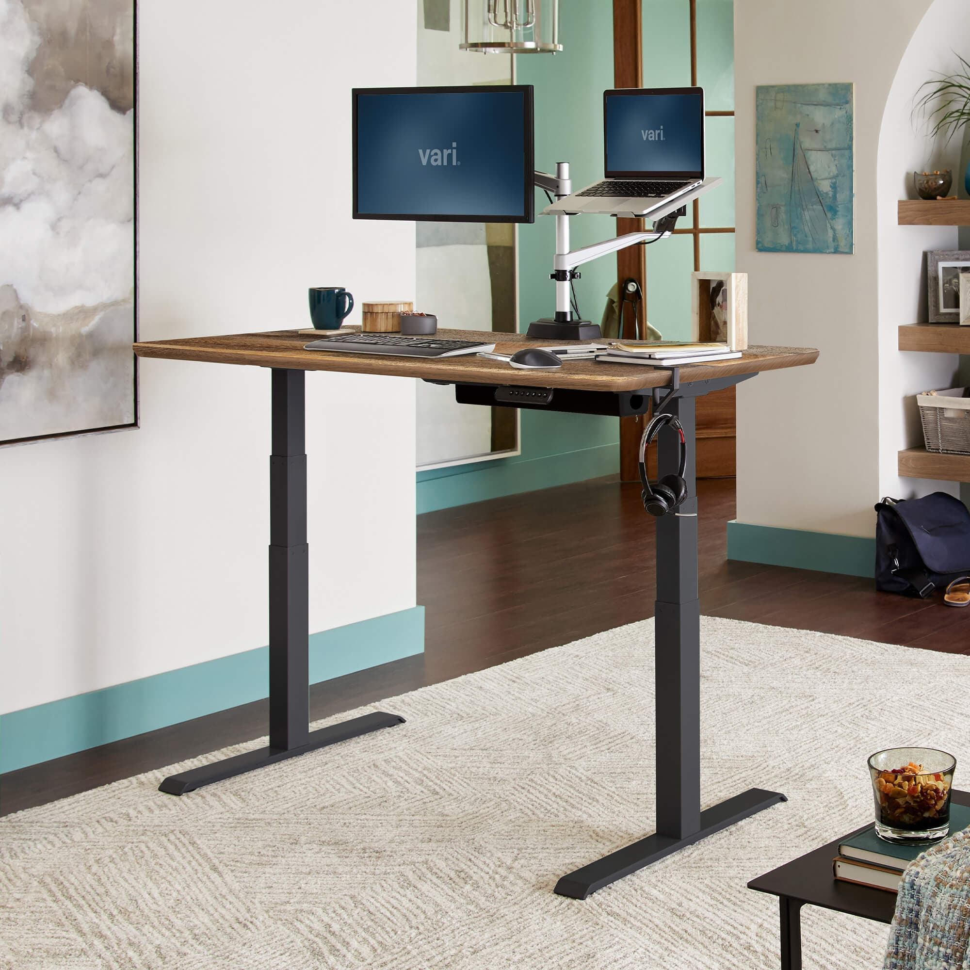 Vari electric standing desk with a wood-look top and black legs, with a monitor and laptop on an arm