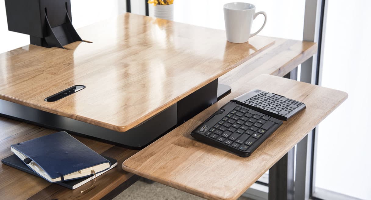 UPLIFT E7 electric desk converter with a wood-look surface and a lower keyboard tray holding a keyboard